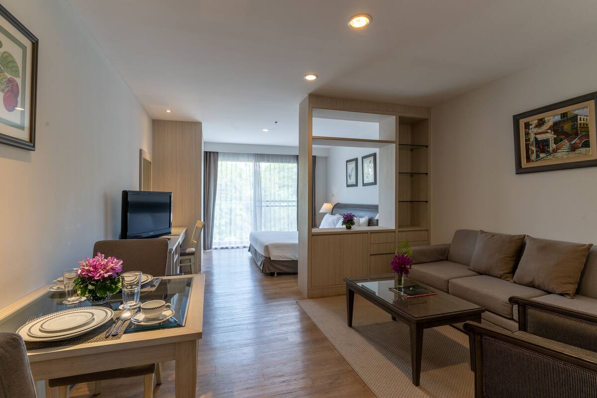 A modern hotel room with a dining area, a sofa, a TV, and a bed.