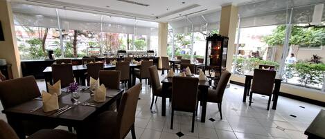 Un restaurante espacioso con techos altos, ventanas amplias y piso de baldosas. Las mesas están dispuestas con sillas y servilletas.
