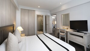 Una habitación de hotel moderna con una cama grande, un escritorio con televisor de pantalla plana, un espejo y un vestidor.