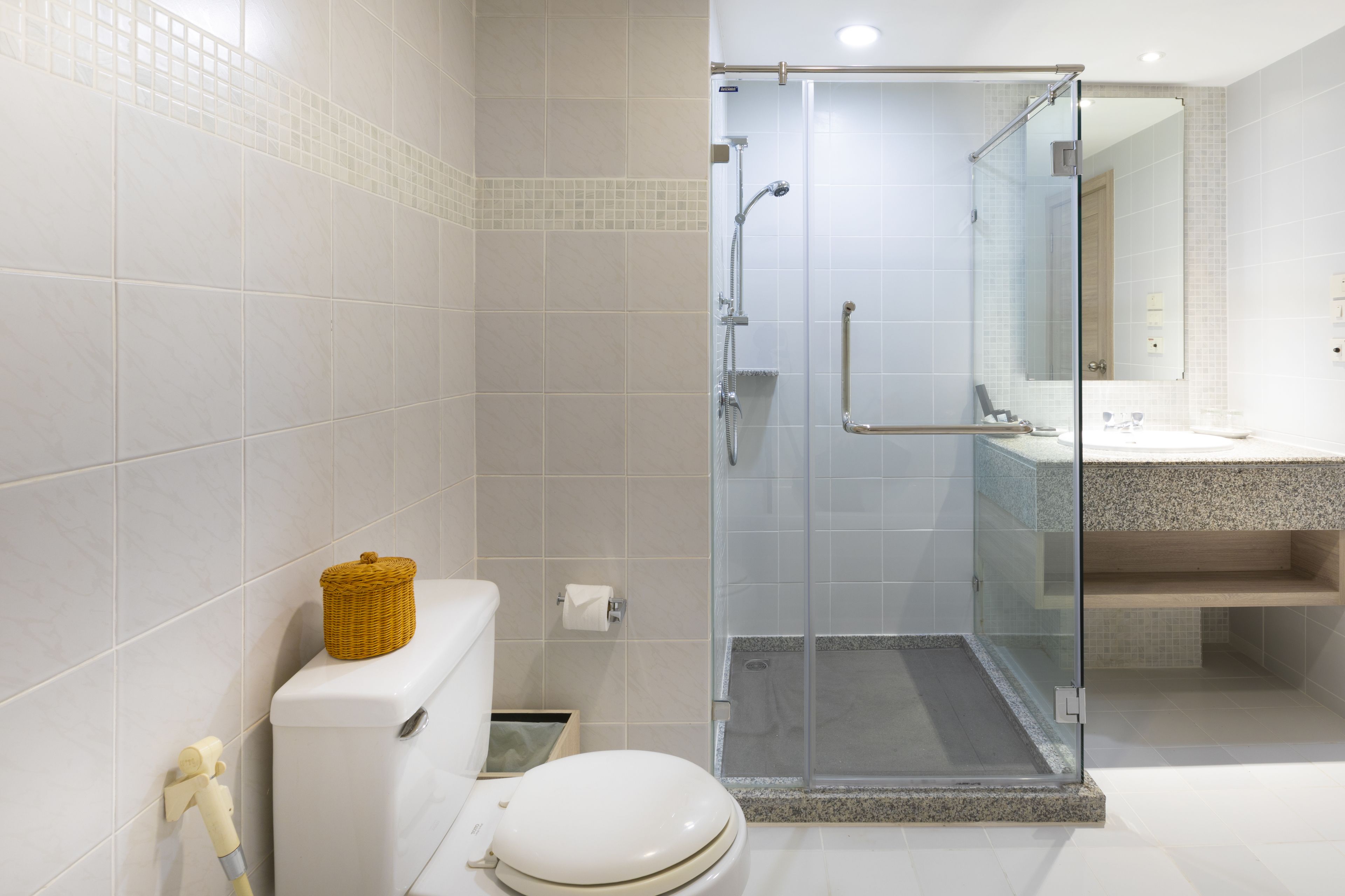 Ein modernes Badezimmer mit einer Glaskabine zur Dusche, einer Toilette und einem Waschbecken mit Spiegel darüber.