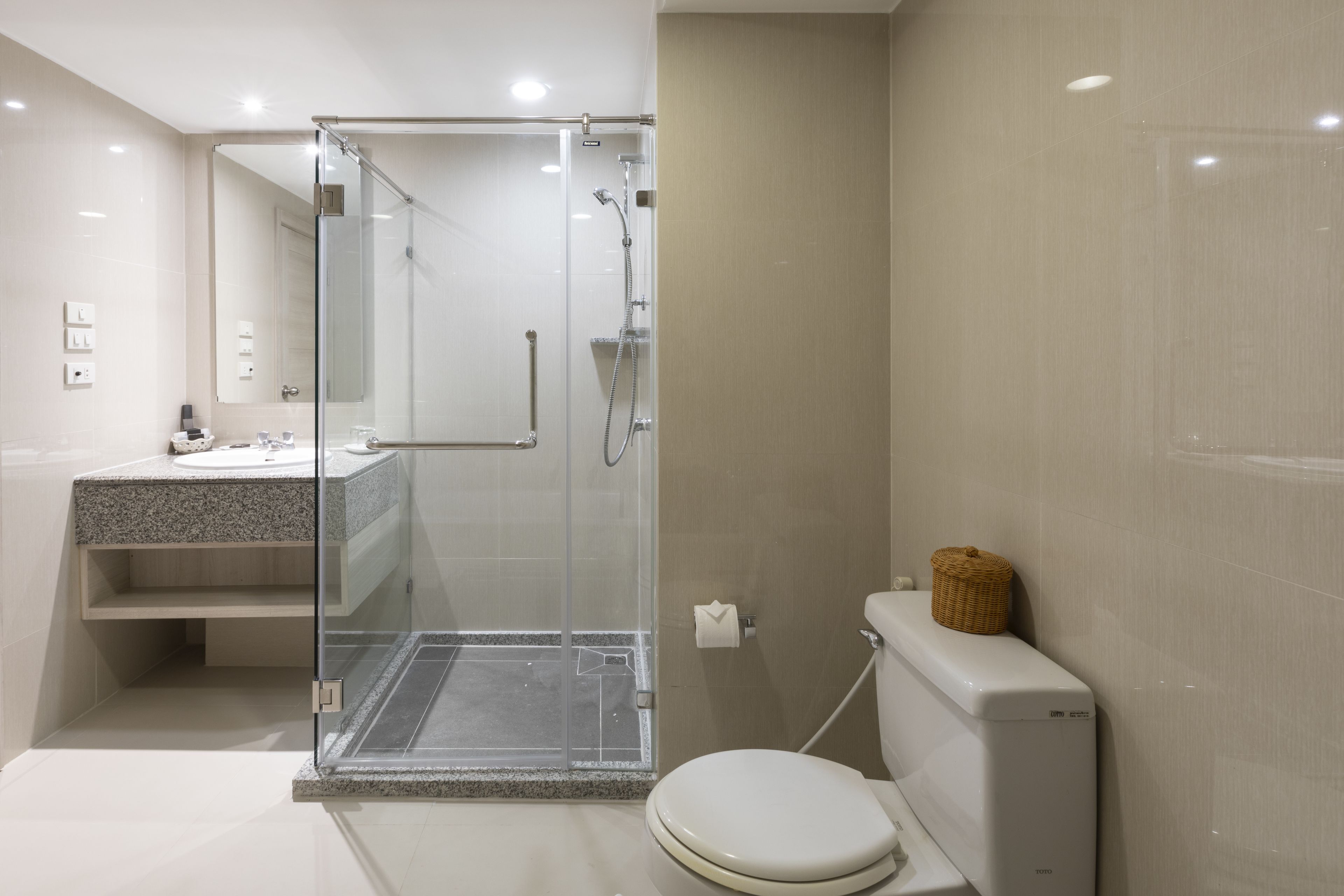 A modern bathroom with a glass-enclosed shower, a white toilet, and a granite countertop sink.