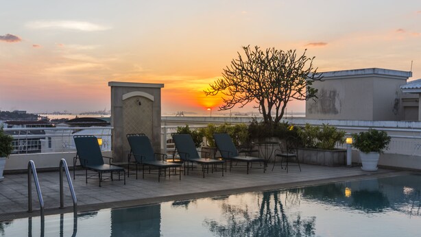 Una piscina en la azotea con sillas de descanso y vistas al atardecer.
