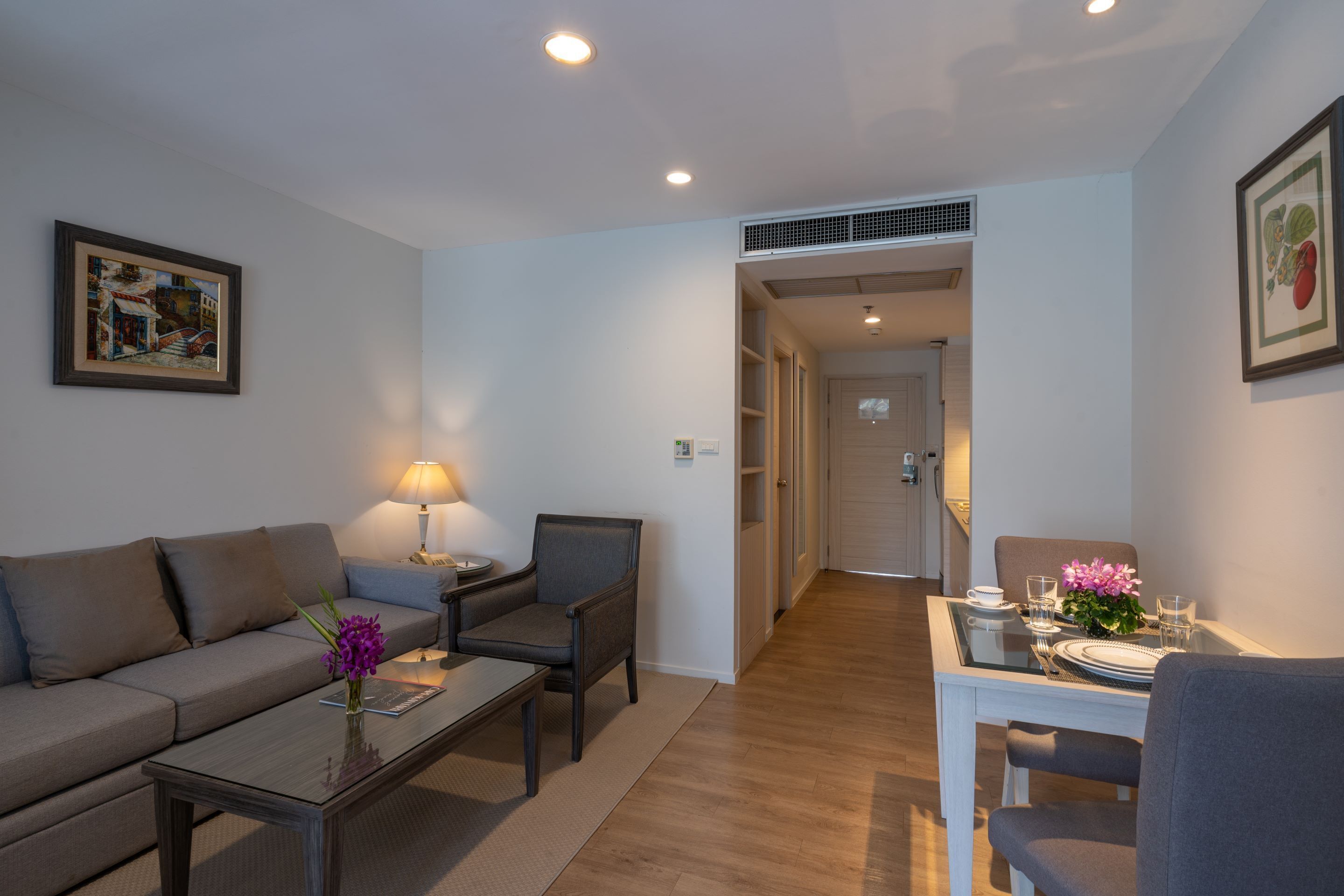 A modern living room with a sofa, armchairs, a coffee table, and a dining area with a table set for two.