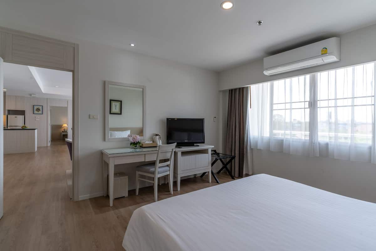 A hotel room with a bed, a desk with a chair, a television, and an air conditioning unit.