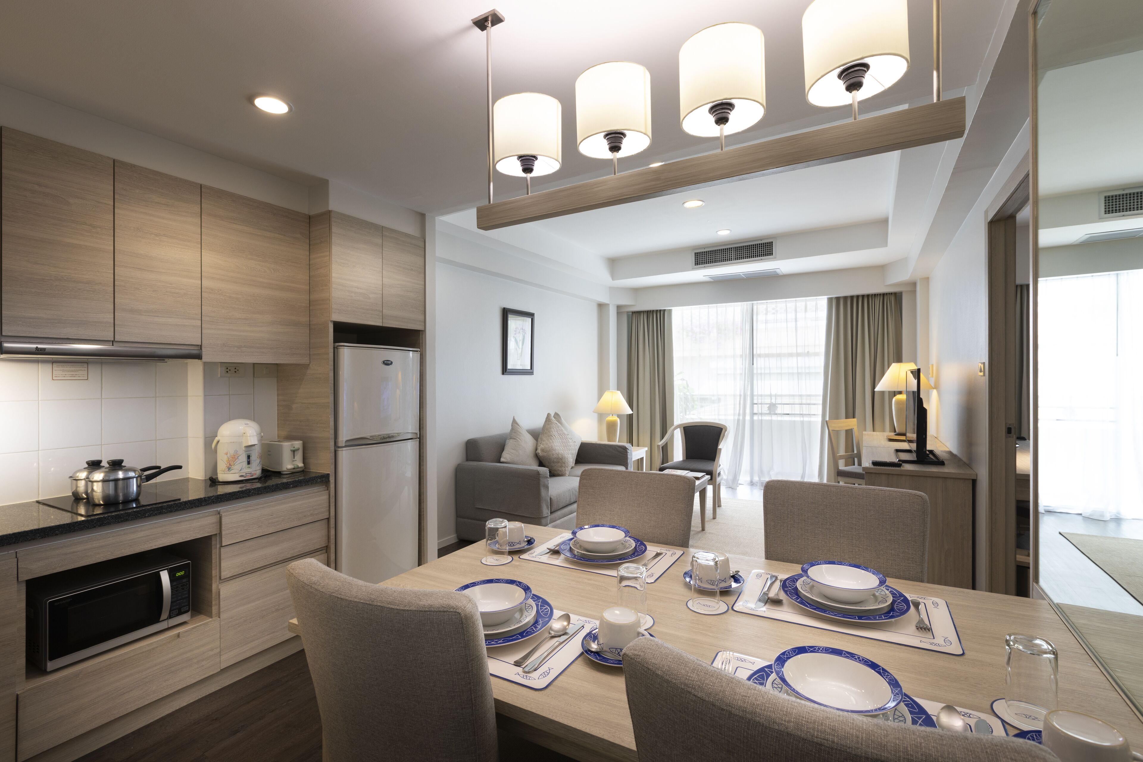 A modern hotel room with a dining area, kitchenette, and a living area with a sofa and lamps.