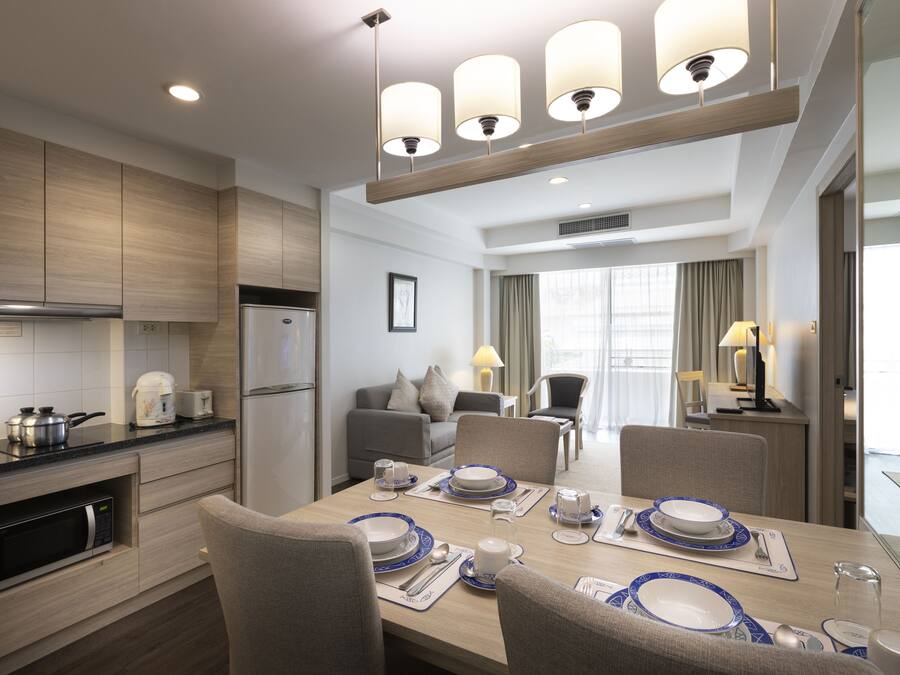 A modern hotel room with a dining area, kitchenette, and a living area with a sofa and lamps.