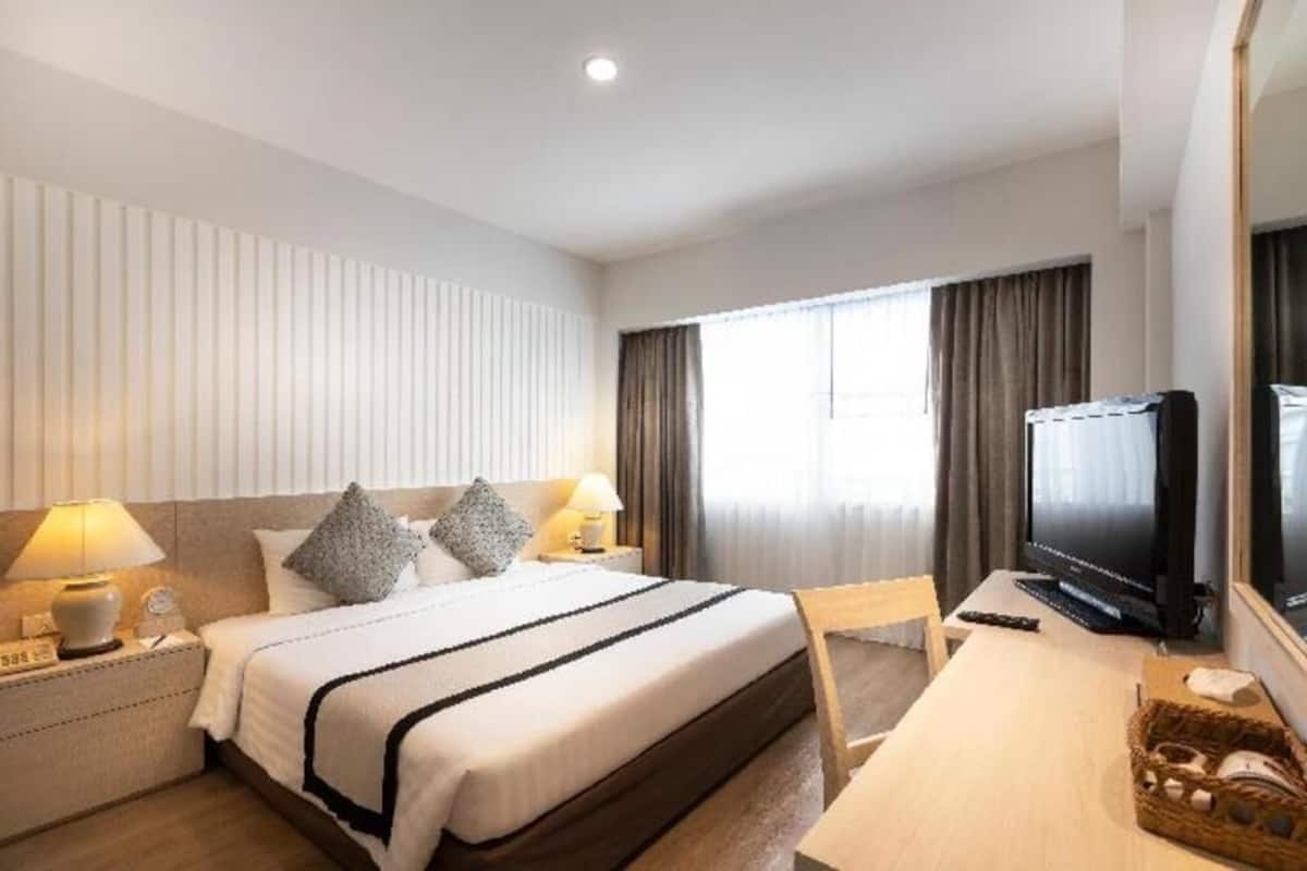 A hotel room with a bed, bedside lamps, a desk with a computer, a television, and a window with curtains.