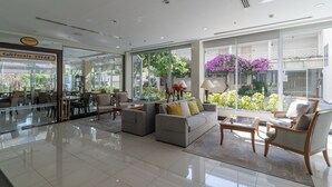 Un amplio vestíbulo con comedor, un conjunto de sofás y grandes ventanales con vistas a follaje y flores.