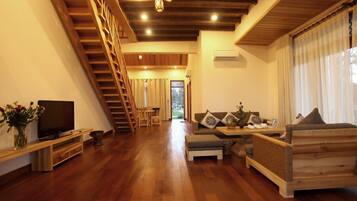 A modern living room with a wooden staircase, a flat-screen TV, a sofa set, and a dining area.
