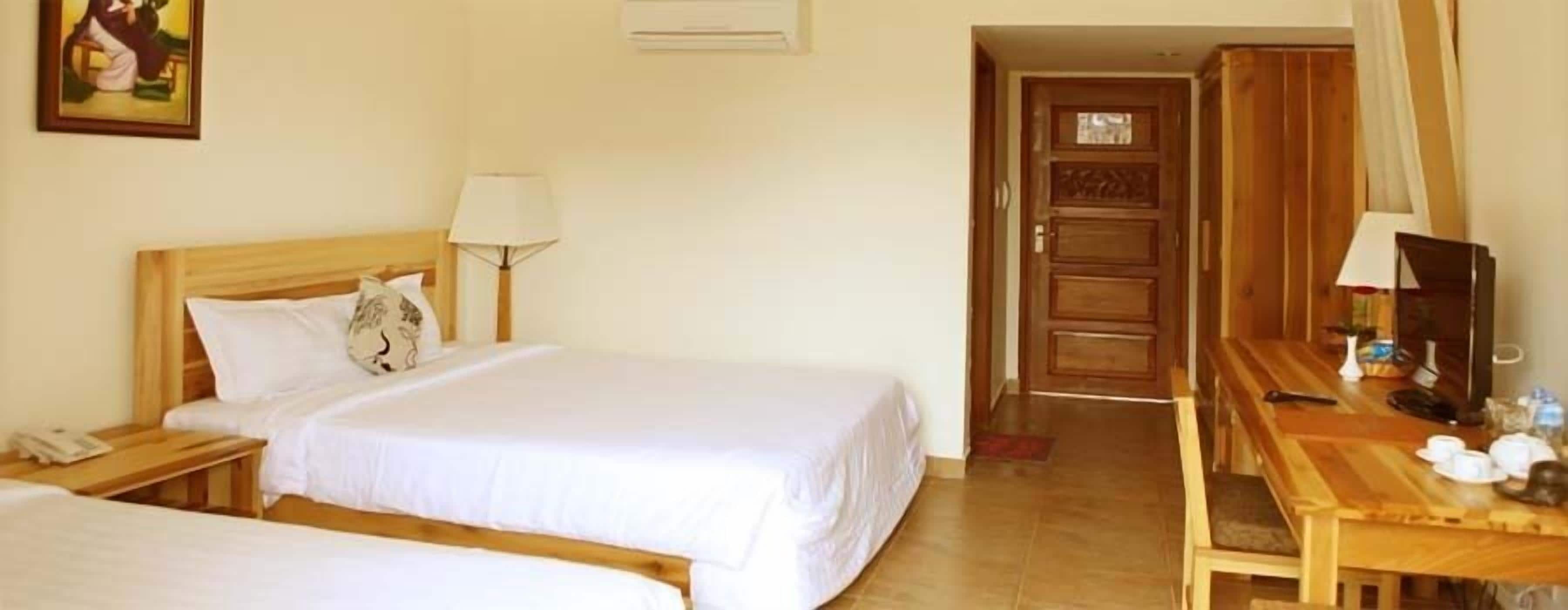 A hotel room with a bed, bedside table, lamp, and a wooden desk with a chair.