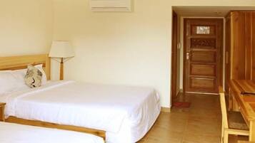 A hotel room with a bed, bedside table, lamp, and a wooden desk with a chair.