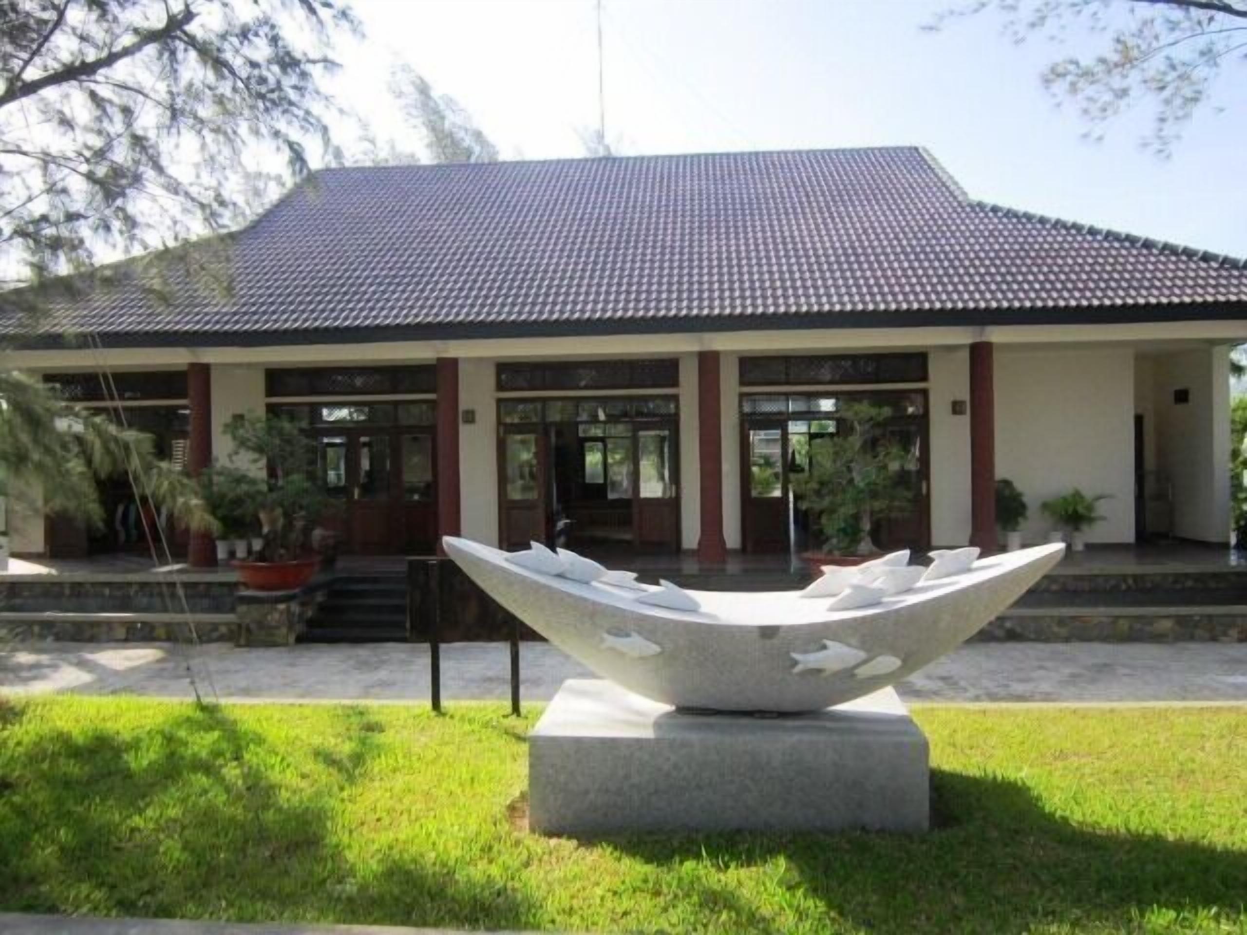 A building with a tiled roof, a large sculpture in front, and potted plants around.