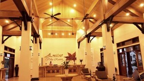 A spacious lobby with wooden beams, a reception desk, seating area, and large windows. - Aniise Villa Resort (Ninh Chu)