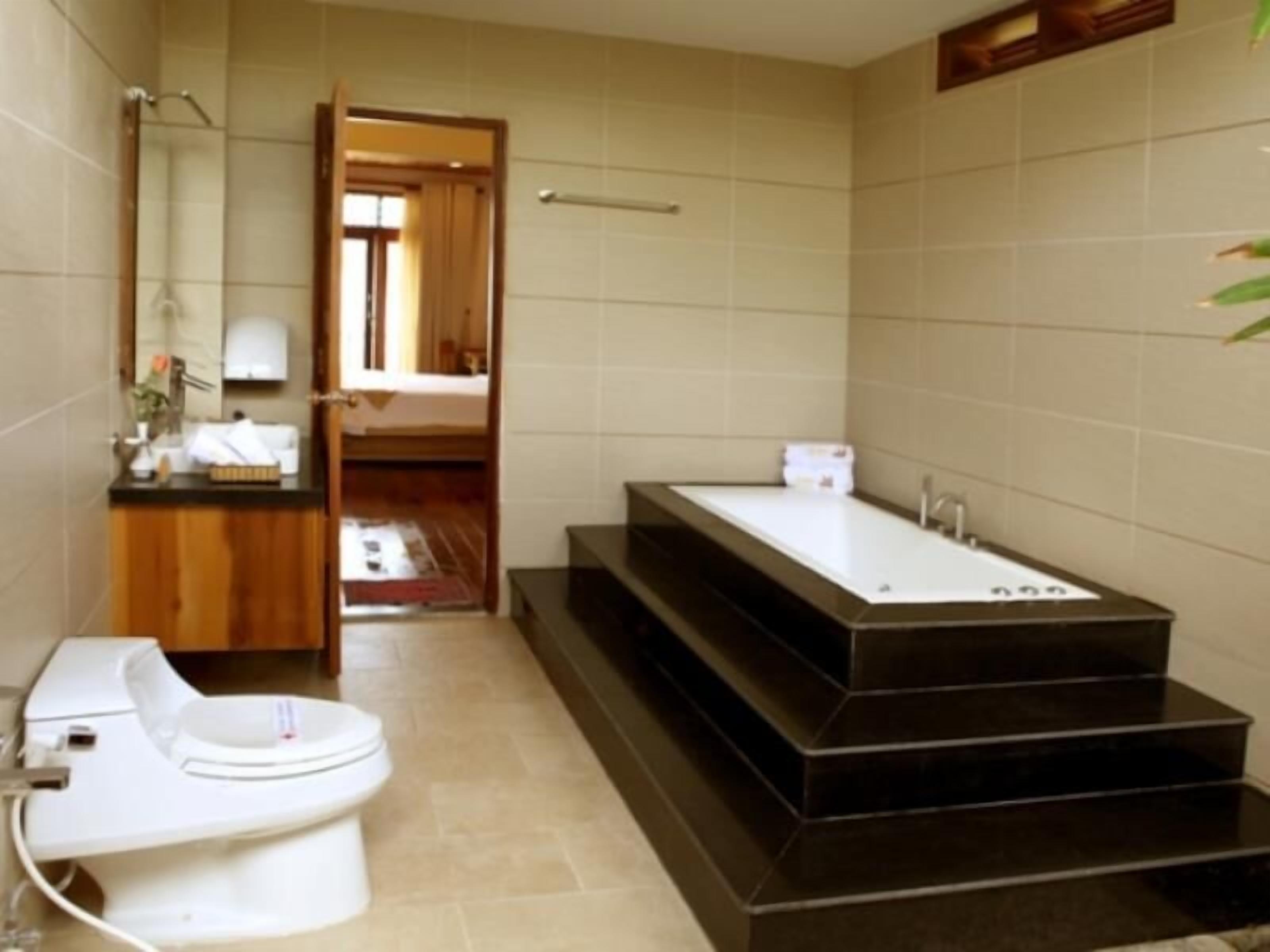 A modern bathroom with a white toilet, a large rectangular bathtub, and a wooden vanity.