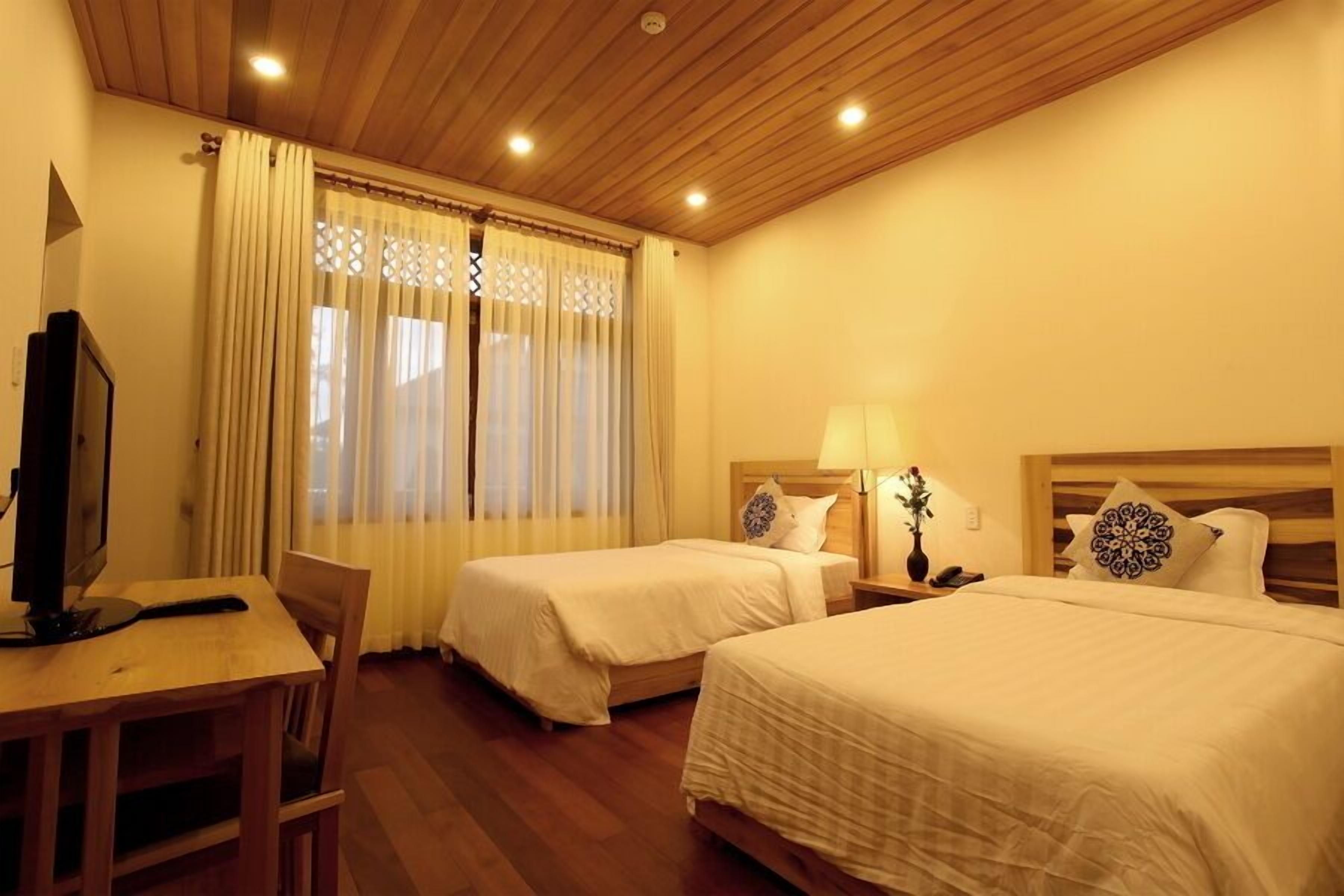 A hotel room with two beds, a desk with a TV, and a wooden ceiling.