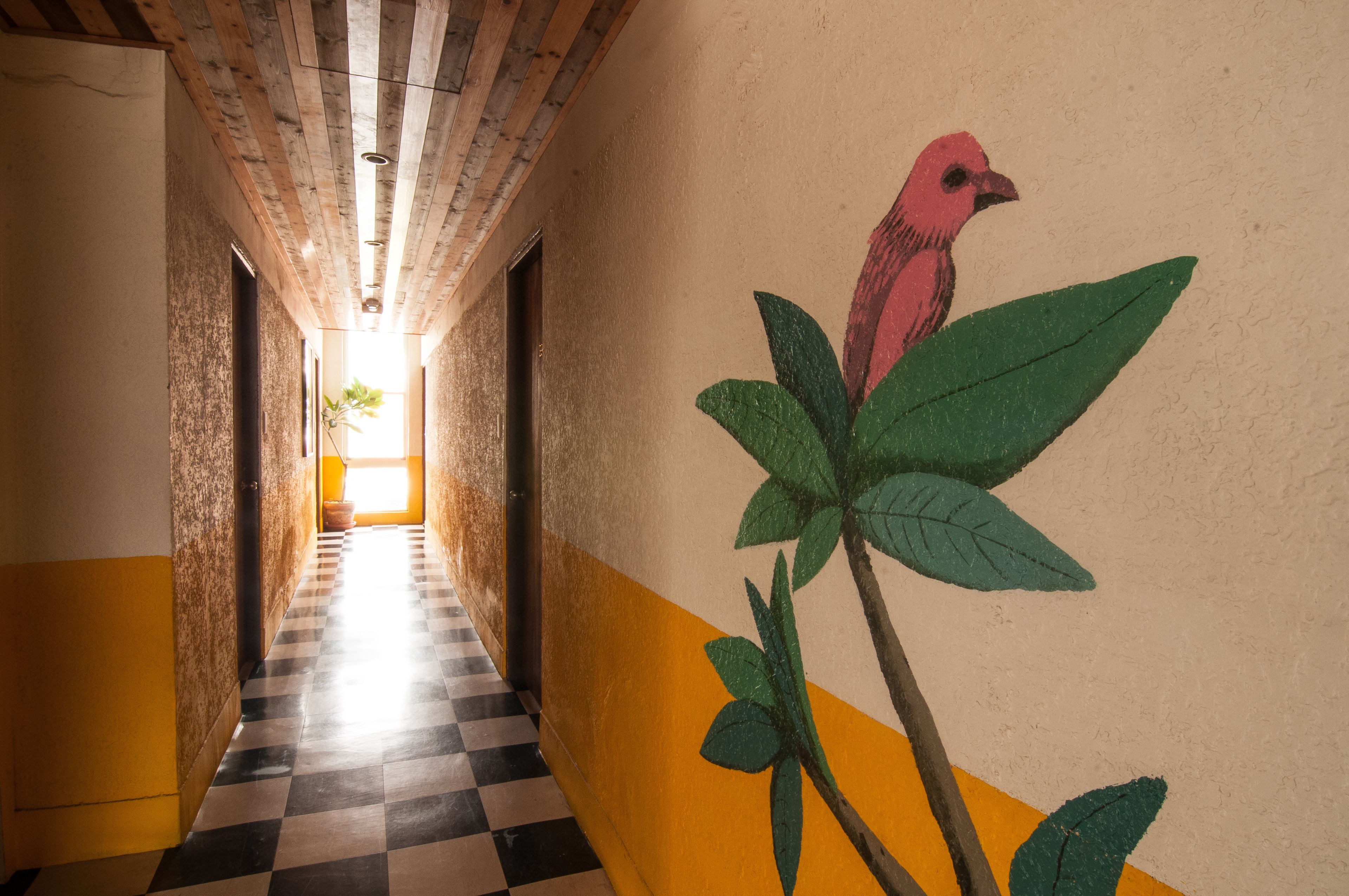 A hallway with a checkered floor, a painted bird on the wall, and a wooden ceiling.