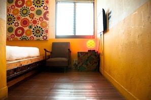 Una habitación con una cama, una silla, un ventanal y una pared con estampado floral.