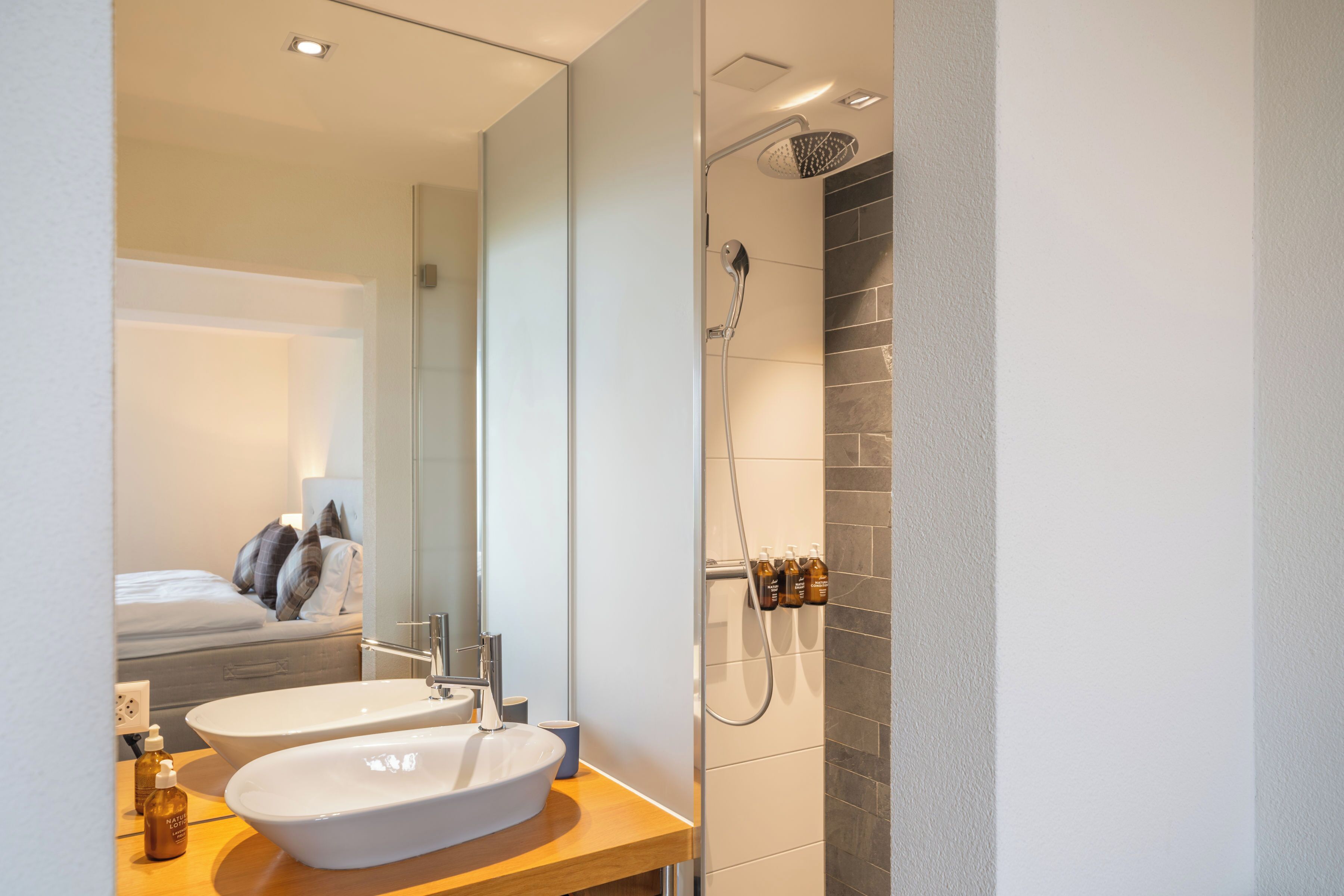 Ein modernes Badezimmer mit einem Doppelwaschbecken, einer Dusche und einem Spiegel.
