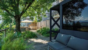 A wooden deck with a sofa, surrounded by lush greenery and a wooden fence.
