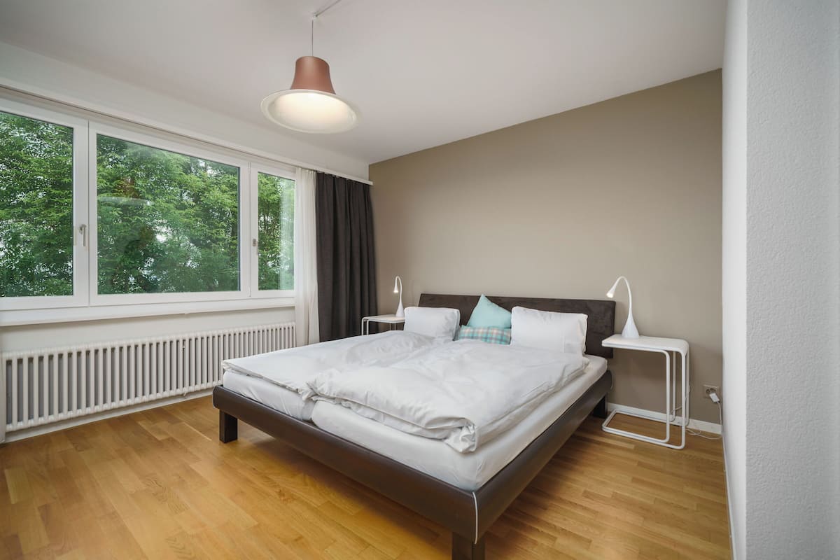 Un dormitorio moderno con un ventanal grande, una cama, mesitas de noche y una lámpara de techo.