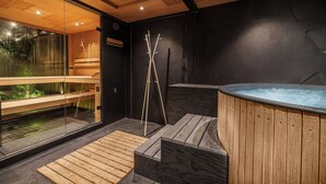 Une salle de spa moderne avec un banc en bois, un jacuzzi et un mur de verre donnant sur un paysage verdoyant.