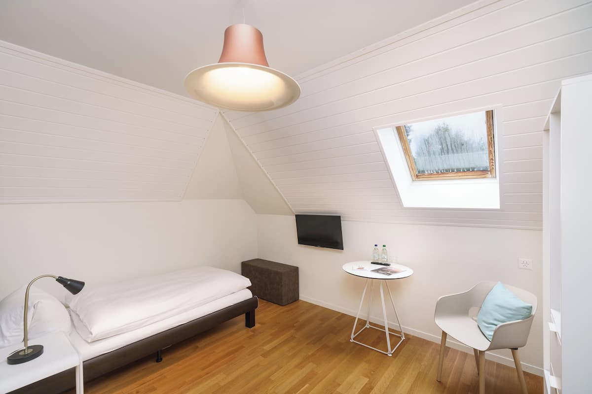 Una habitación compacta con cama, una mesita, una silla, un televisor y una ventana.