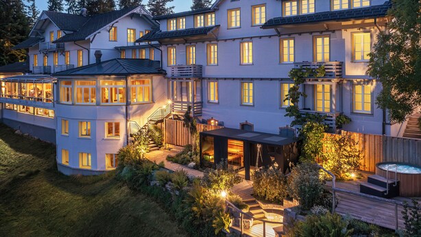 Un grand bâtiment à étages doté d’un vaste patio extérieur bien éclairé, d’un jacuzzi et d’une terrasse en bois.