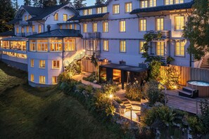 A large, multi-story building with a well-lit outdoor patio area, a hot tub, and a wooden deck. - Boutique Hotel Moosegg (Lauperswil)