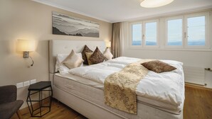 Une chambre à coucher avec un grand lit, une tête de lit, une table de chevet, une lampe, un tableau et une fenêtre avec des rideaux.