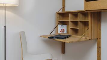 Ein schlichter Raum mit einem weißen Stuhl, einem Holztisch mit Ablagefläche und einer Lampe.