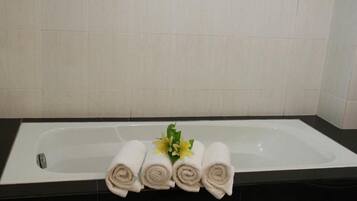 Un baño con una bañera, tres toallas enrolladas y un pequeño arreglo floral.