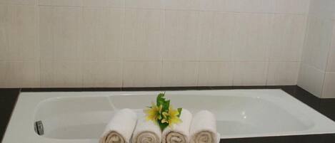 Un baño con una bañera, tres toallas enrolladas y un pequeño arreglo floral.