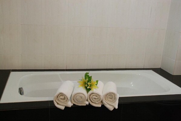 A bathroom with a bathtub, three rolled towels, and a small flower arrangement.