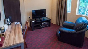 A room with a bed, a TV on a stand, a coffee table, a leather chair, and a window with curtains. - Grandview Hotel (Raub)