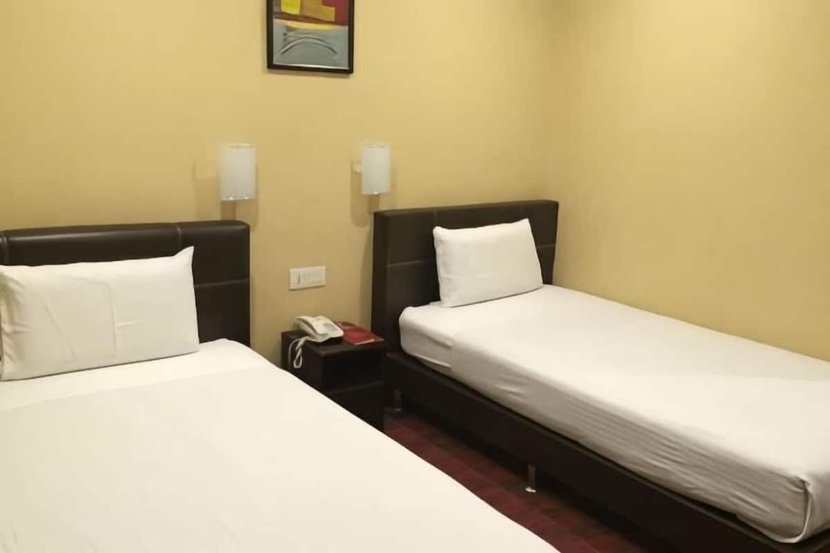 A hotel room with two single beds, a nightstand with a phone, and a wall-mounted lamp.