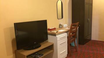 A hotel room with a TV on a wooden stand, a desk with a chair, a mirror, and a wardrobe.