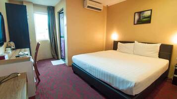 A hotel room with a bed, a desk, a chair, an air conditioning unit, and a painting on the wall.