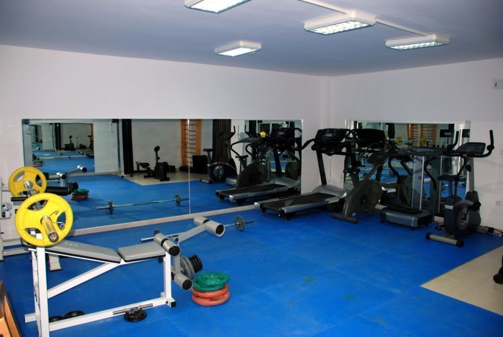 A gym with exercise equipment, mirrors, and blue flooring.