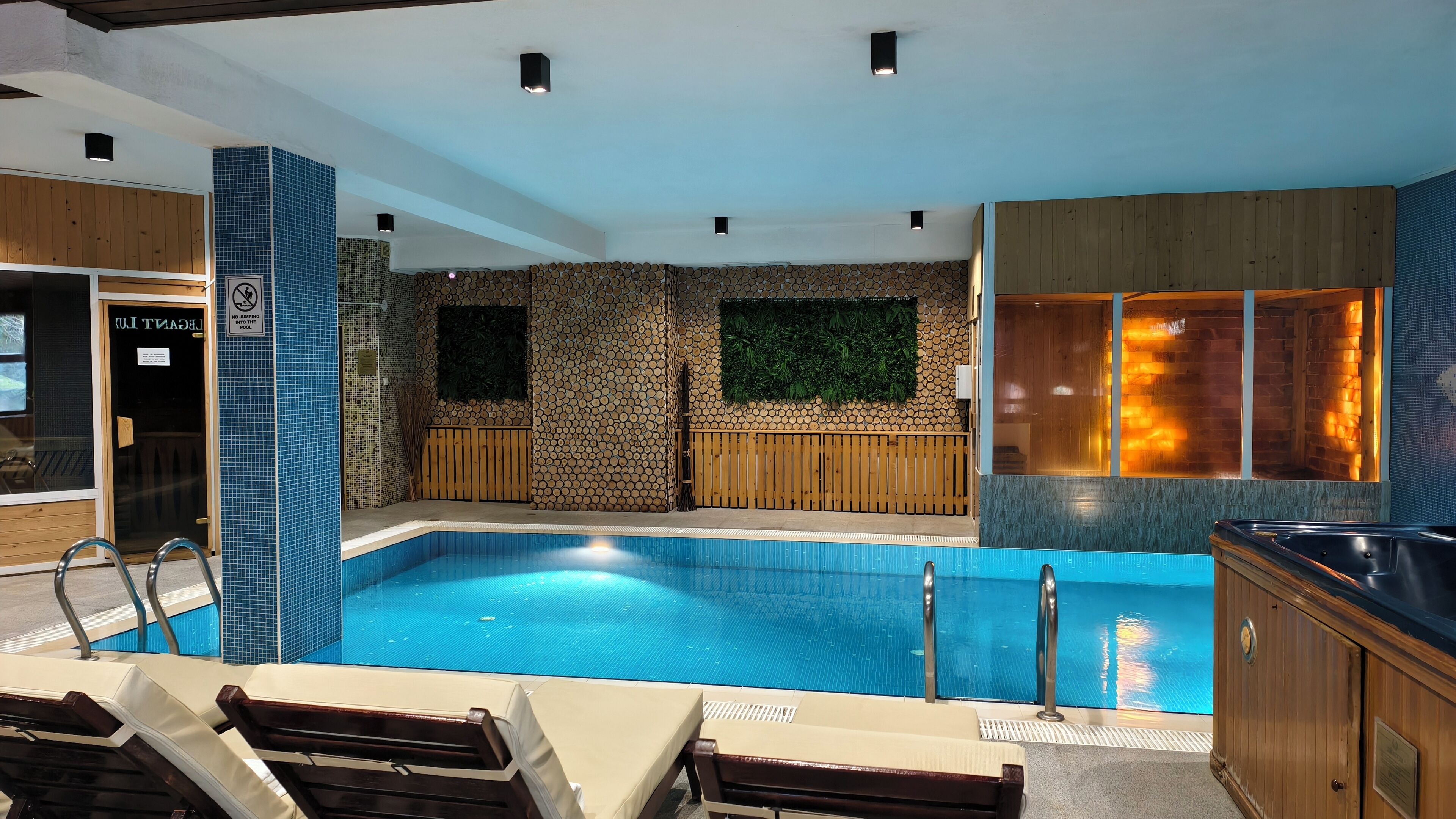 Uma área interna de piscina moderna, com piscina transparente, bancos de madeira e espaço para sauna.