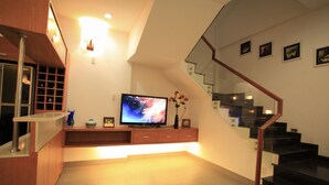 Ein modernes Wohnzimmer mit einem Flachbildfernseher, Holzschränken, einer Glasstufenkonstruktion und gerahmten Bildern an der Wand.