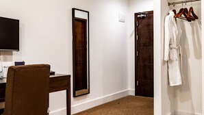 Habitació d'hotel amb escriptori de fusta, un gran mirall, un armari amb albornoz i una porta que dóna a un bany.