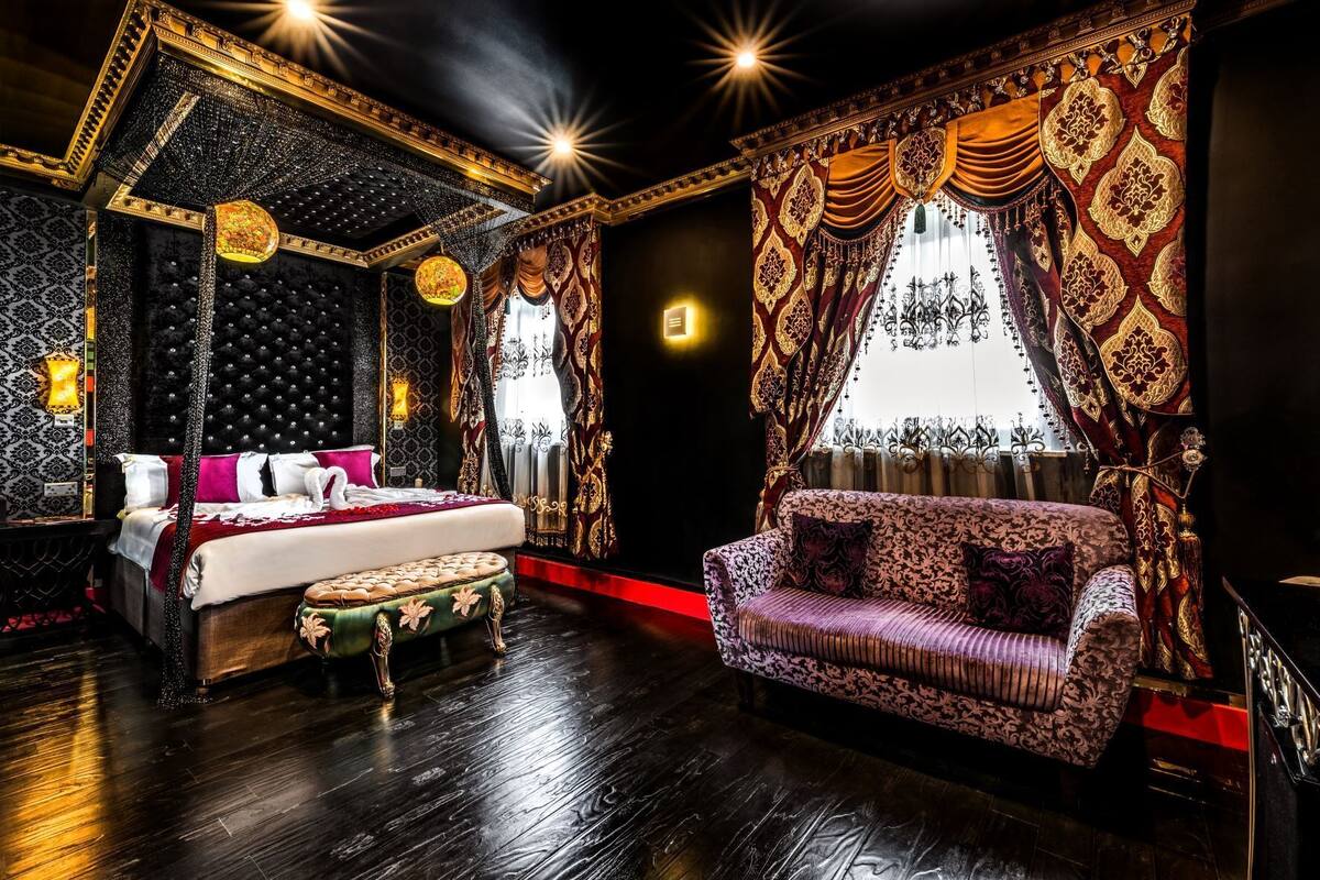 A luxurious bedroom with a large bed, a chaise lounge, and ornate curtains.