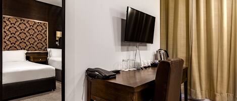 A hotel room with a bed, a desk with a telephone, a flat-screen TV, and a curtain.