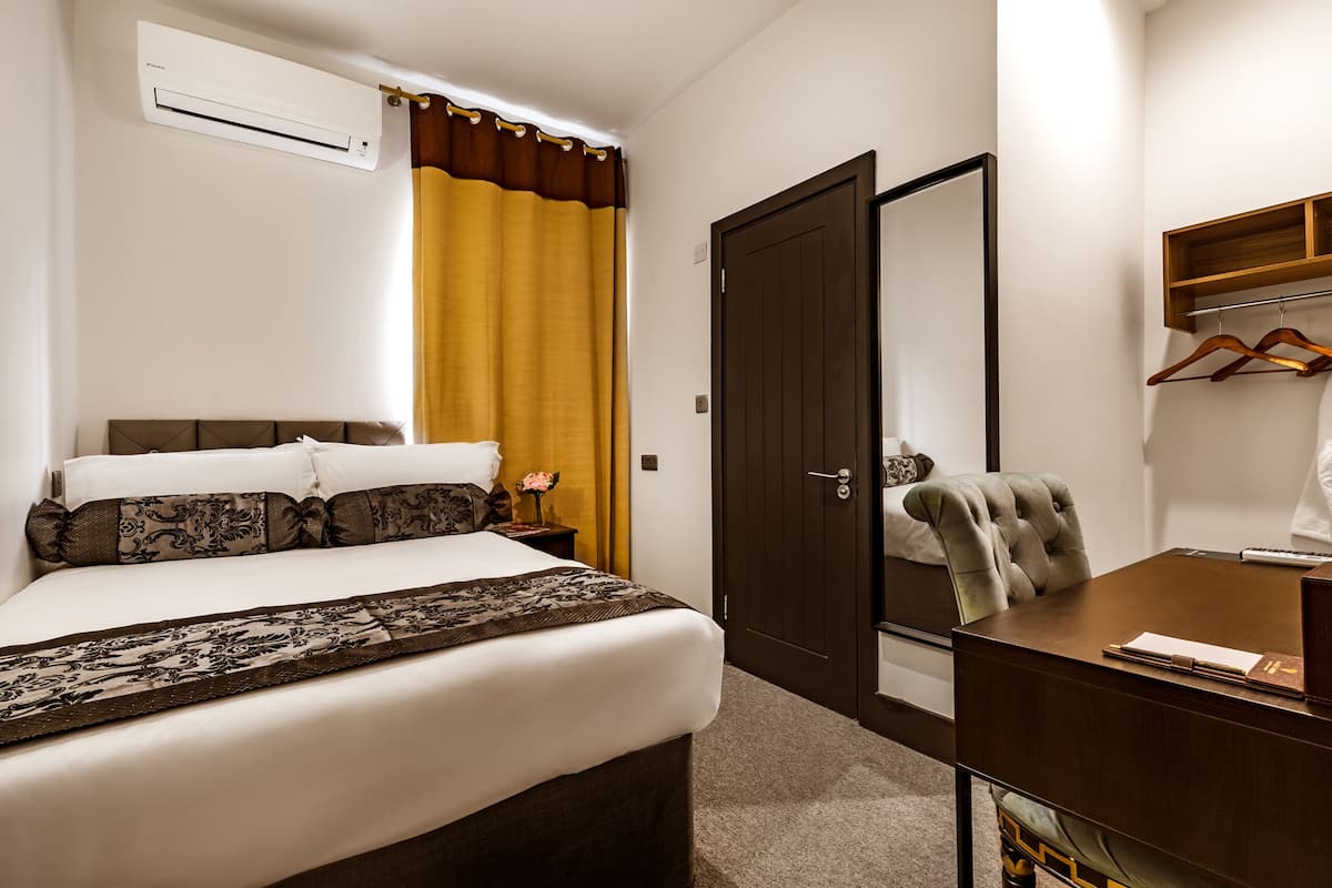 A hotel room with a bed, a desk, a chair, a wardrobe, and a mirror.