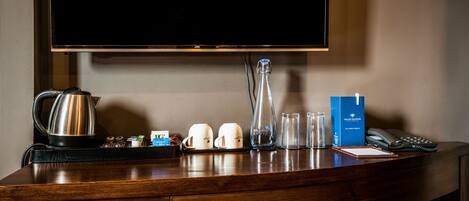 Un mostrador de recepción de hotel con un televisor de pantalla plana, una cafetera, tazas, vasos, un teléfono y un folleto de Grand Millennium.