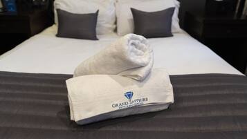 A neatly made bed with a folded towel and a blanket, a dark headboard, and a patterned wall.
