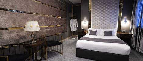 Ett modernt hotellrum med en stor säng, en sittgrupp med en lampa och en badrock som hänger på väggen.