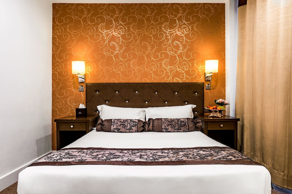 A neatly made bed with a patterned bedspread, two bedside lamps, and a decorative headboard.