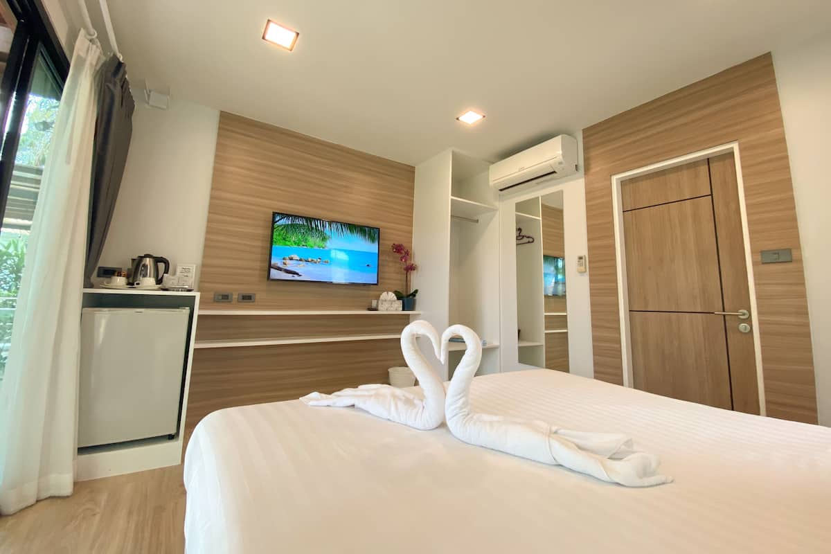 A hotel room with a bed, a TV, a desk with a kettle, and a wardrobe.
