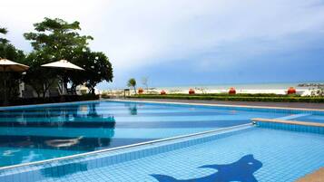 A swimming pool with a dolphin tile design, surrounded by lounge chairs and umbrellas, with a view of the beach and ocean.